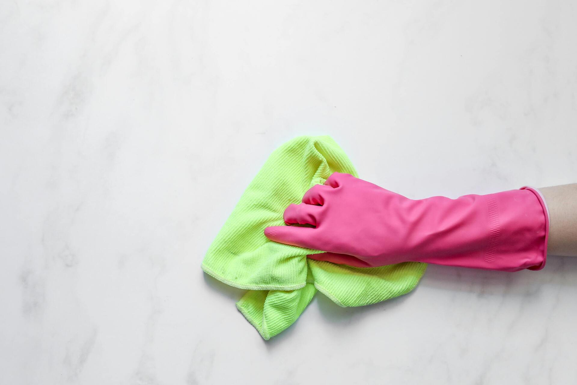 An image of a hand wearing gloves holding a cleaning cloth.