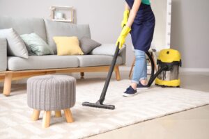 A person wearing yellow gloves cleaning the house floor using a vacuum cleaner.