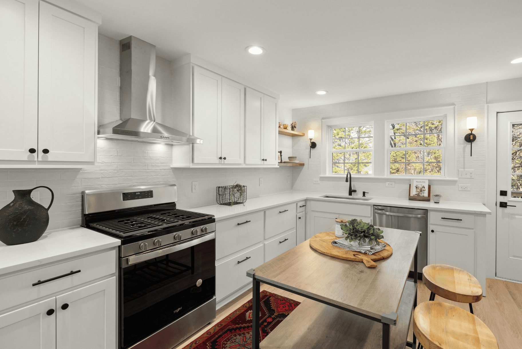 Bright kitchen with white cabinets, stainless steel stove, and a small wooden island.