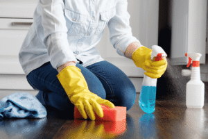 A person cleaning a bathroom floor with a sponge and cleaning products